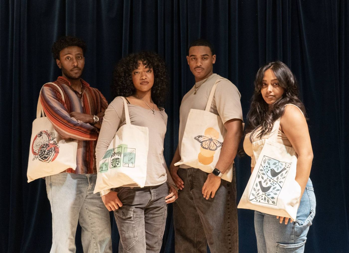 Four people holding Angaza Taa tote bags printed with a pomegranate, leaves, a butterfly and birds