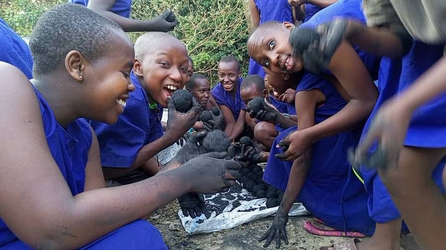 Smiling students with blackened hands rolling charcoal briquettes