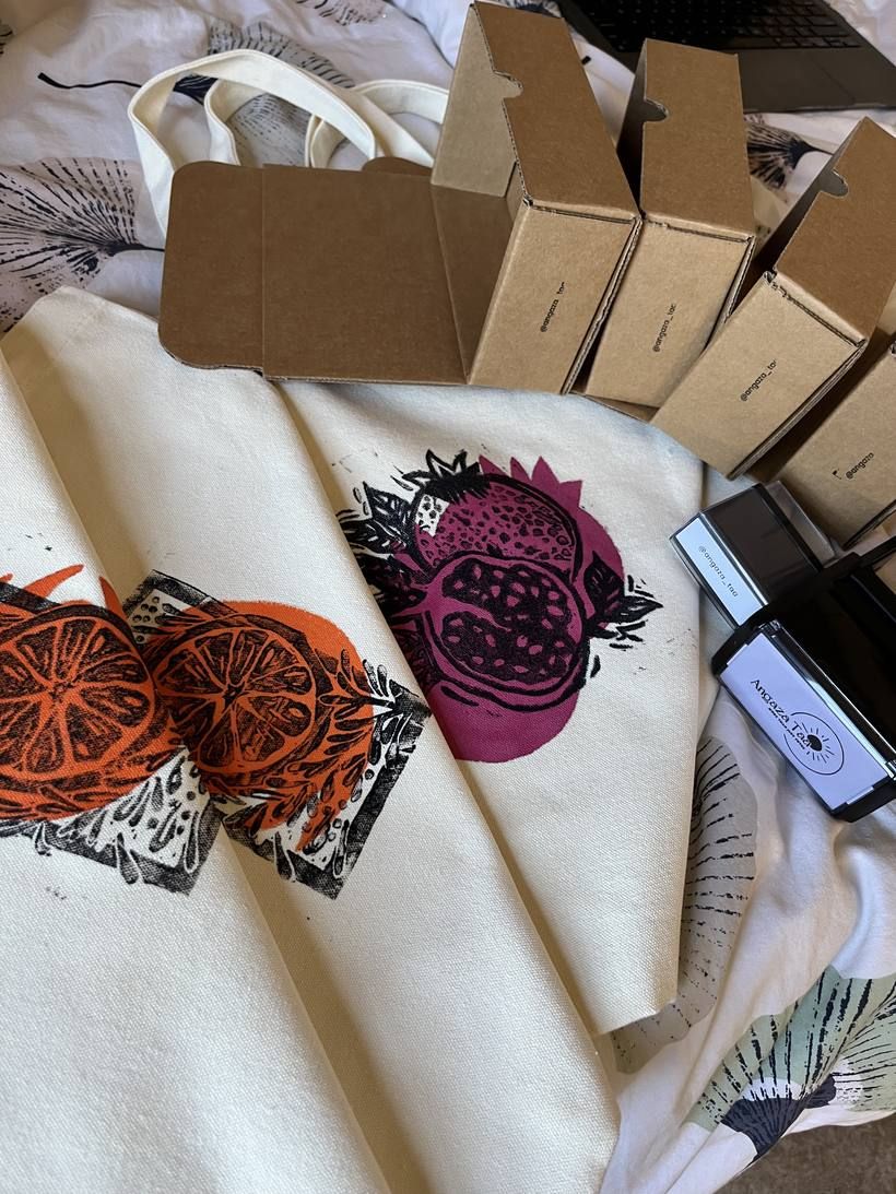 Block-printed citrus and pomegranate totes laid out beside Angaza Taa shipping boxes
